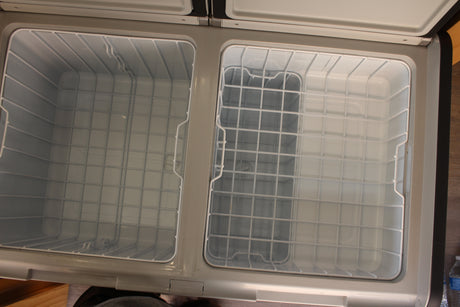 Clean, empty dual-zone portable refrigerator/freezer, ideal for your RV rental. Features white wire baskets for organized storage.