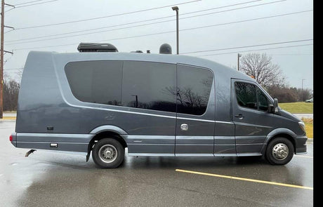 Customized dark grey RV rental van with tinted windows & roof AC, parked on a wet lot. Ideal for road trips.
