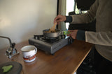 RV rental life: Preparing a meal on a compact stove in a functional camper kitchen. Features an enamel mug.