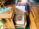 Smart RV rental interior featuring a hidden pull-out toilet, custom wooden counter with ocean art, & compact sink.