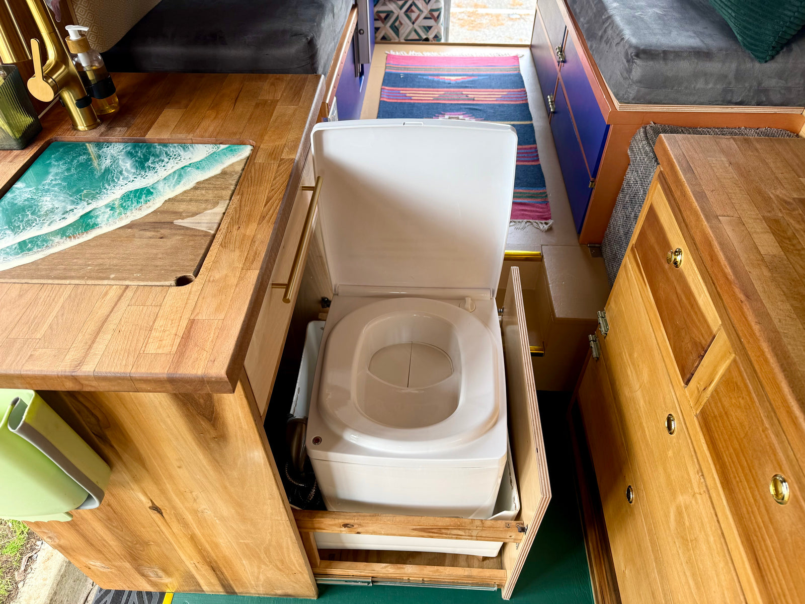 Smart RV rental interior featuring a hidden pull-out toilet, custom wooden counter with ocean art, & compact sink.