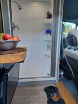 This RV rental interior features a functional shower, dog food station, TV, and fruit, offering comfort on the road.