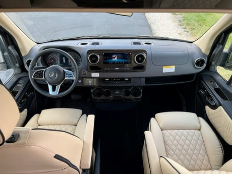 RV rental: Mercedes-Benz Sprinter van's luxurious front cabin. View of dashboard, steering wheel, and light quilted leather seats.