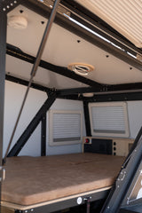 Cozy RV rental interior with a comfortable bed, small windows, and an overhead fan, ready for your next adventure.