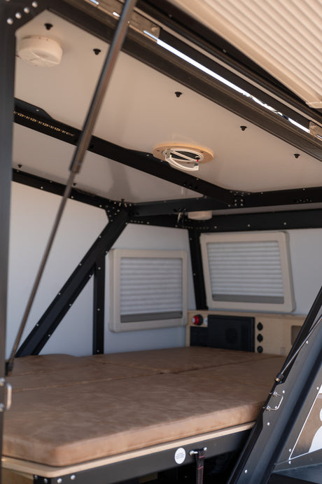 Cozy RV rental interior with a comfortable bed, small windows, and an overhead fan, ready for your next adventure.