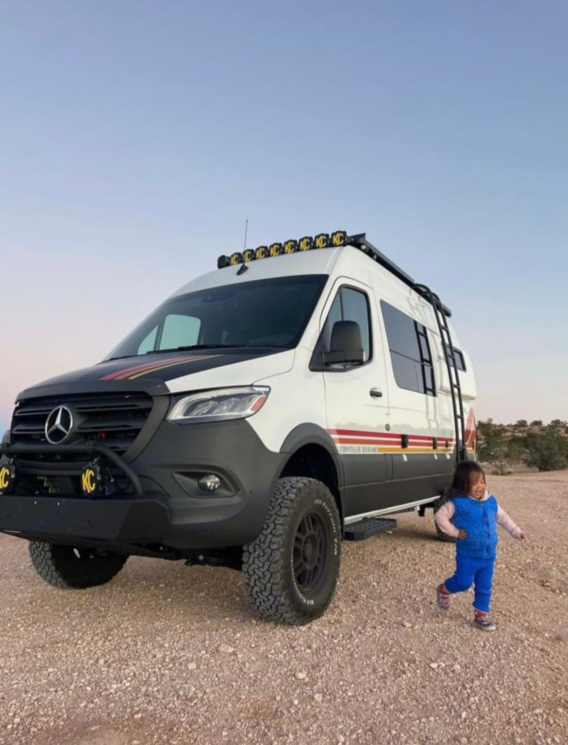 Off-road Mercedes Sprinter **RV rental** for adventure! A child plays near this rugged camper van on a dirt road.