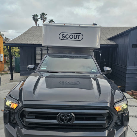 Dark grey Toyota truck, an RV rental, with a white 'SCOUT' truck camper unit. Parked outdoors.