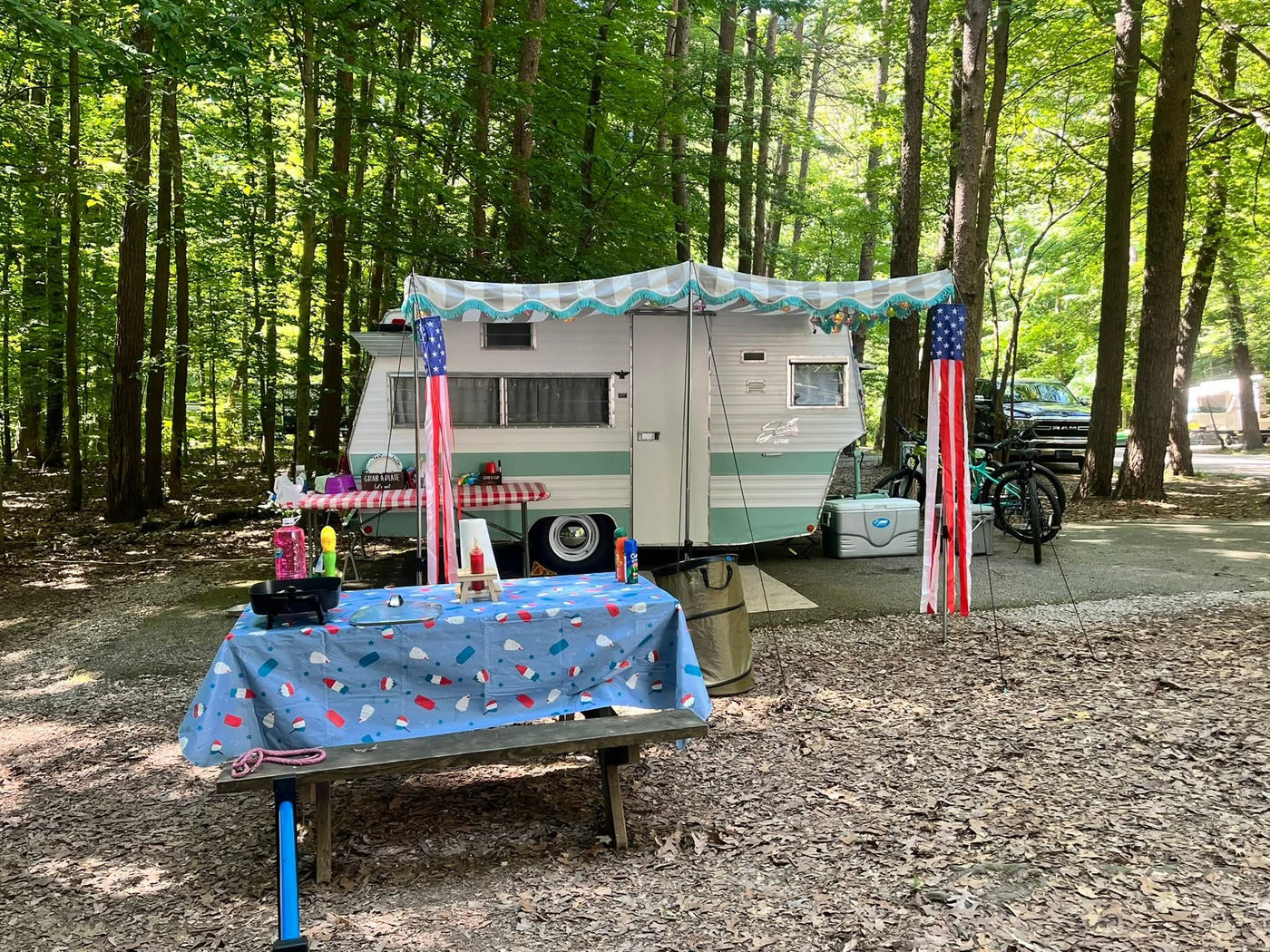 Charming RV rental camper under a festive awning with picnic tables in a serene woodland campsite. — photo 11