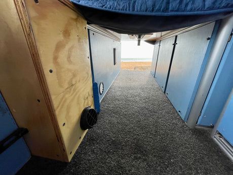 Inside an rv rental: carpeted aisle, wooden under-bed storage, and blue side panels lead to a scenic beach view.