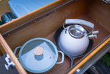 RV rental kitchen essentials: A teal pot, white kettle on cast iron pan, and thermos neatly stored in a wooden drawer.