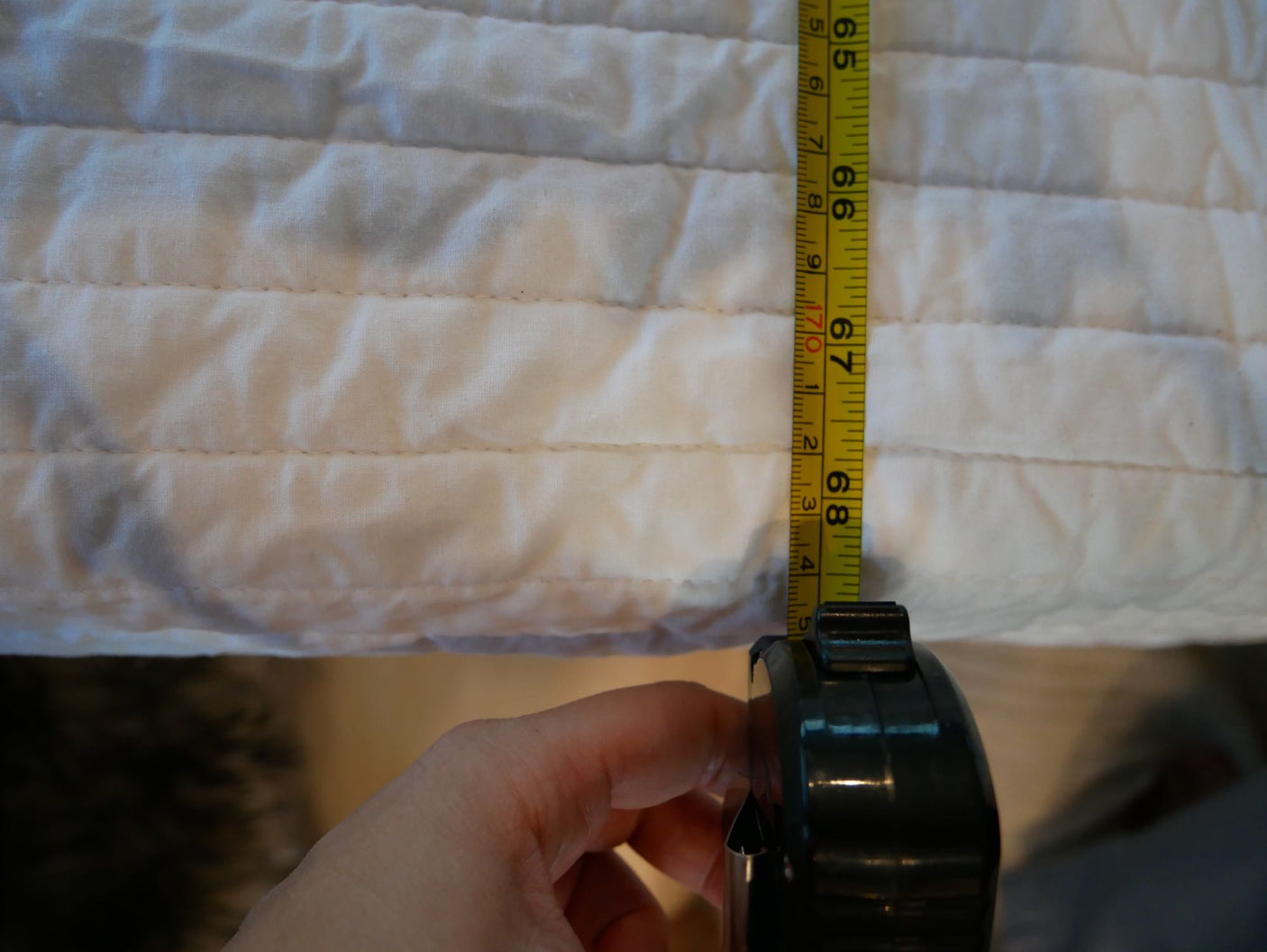 Hand measures quilted fabric to 68.4 cm for an RV rental, ensuring accurate dimensions for a comfortable space.