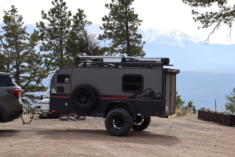 This rugged RV rental off-road camper is hitched to an SUV, set against majestic snowy mountains and pine trees. — photo 12