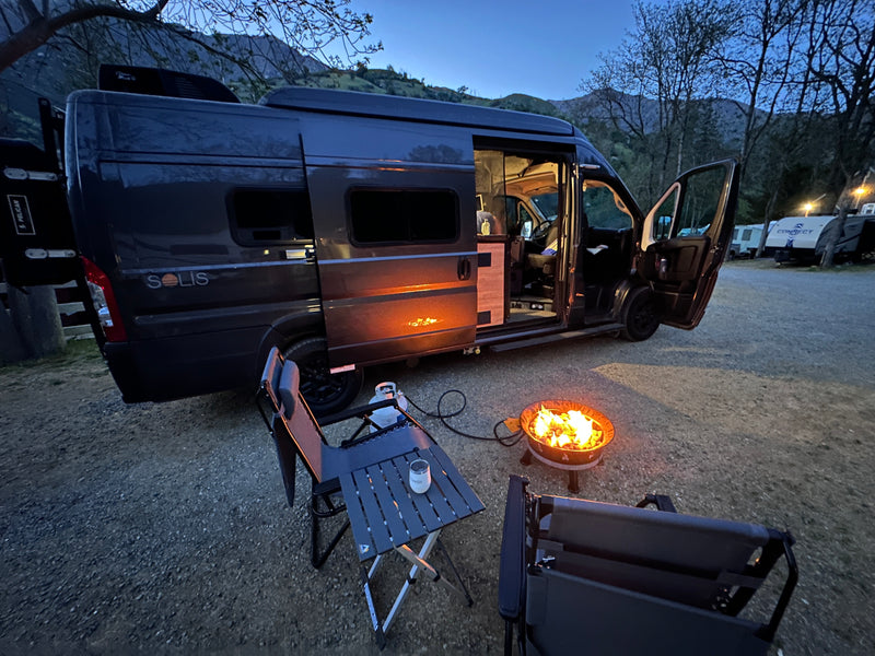 Solis RV rental parked at dusk in a mountain campsite, with a cozy propane campfire, table, and chairs set up for relaxation. — photo 10