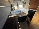 Cozy rv rental van interior: a comfortable bed at the back, counter with stovetop, and storage ideal for compact mobile living.