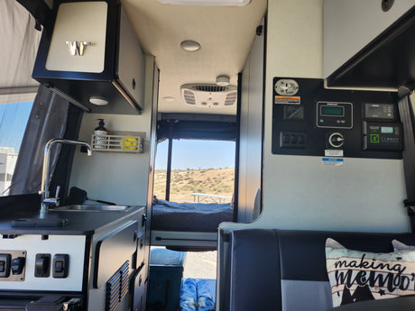 Spacious RV rental interior with kitchen, control panel, and scenic desert view from the rear bed area. Perfect for a road trip.