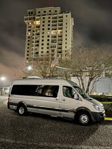 A silver Airstream RV rental van is parked on a cobblestone street at night, featuring a tall building and trees.