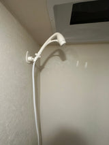 Compact RV rental shower featuring a white handheld showerhead and hose mounted to a wall.