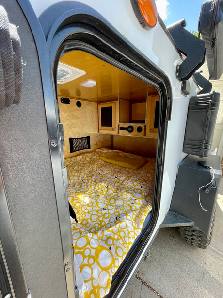 Step inside this cozy RV rental! A bed with bright yellow sheets fills the compact, wood-paneled interior of a camper.