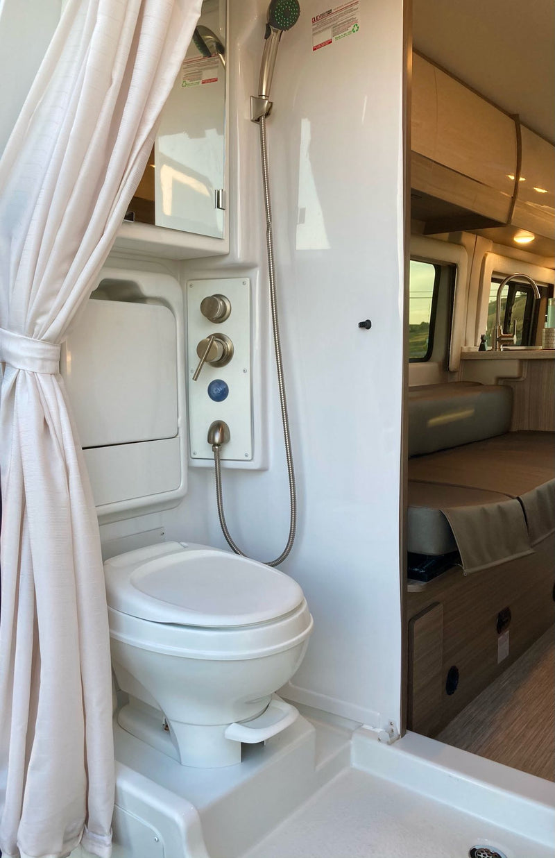 RV rental interior featuring a compact bathroom with shower, toilet, and adjacent living space. — photo 9