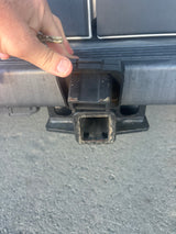 Hand with a key near an RV rental vehicle's trailer hitch receiver, crucial for secure towing.