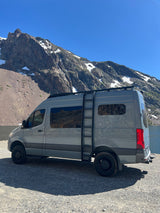 Grey camper van, great for an RV rental adventure, parked by a scenic mountain lake under a clear sky.