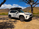 This white SUV, equipped with a Roofnest rooftop tent, is ready for your RV rental adventure on sandy terrain with mountains.