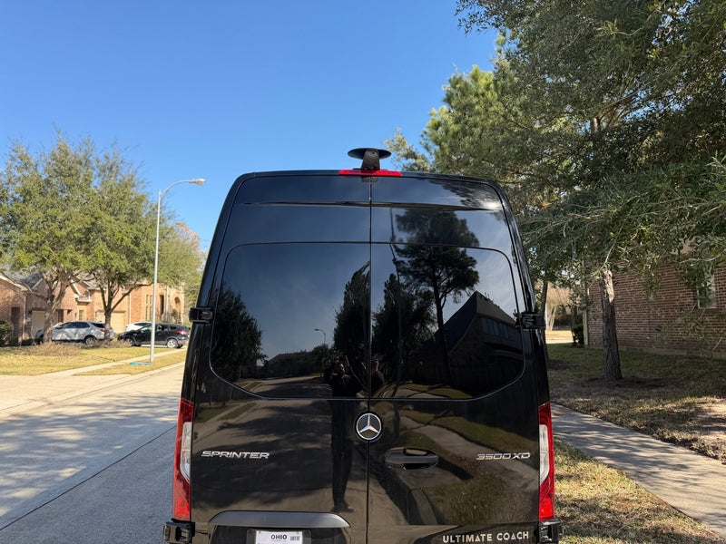 Black Mercedes-Benz Sprinter van, an Ultimate Coach perfect for rv rental, parked on a sunny street reflecting trees and houses. — photo 6