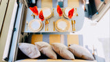 Elegant dining in an RV rental: golden cutlery, chic plates, red napkins, and comfy seat cushions create a luxurious travel space.