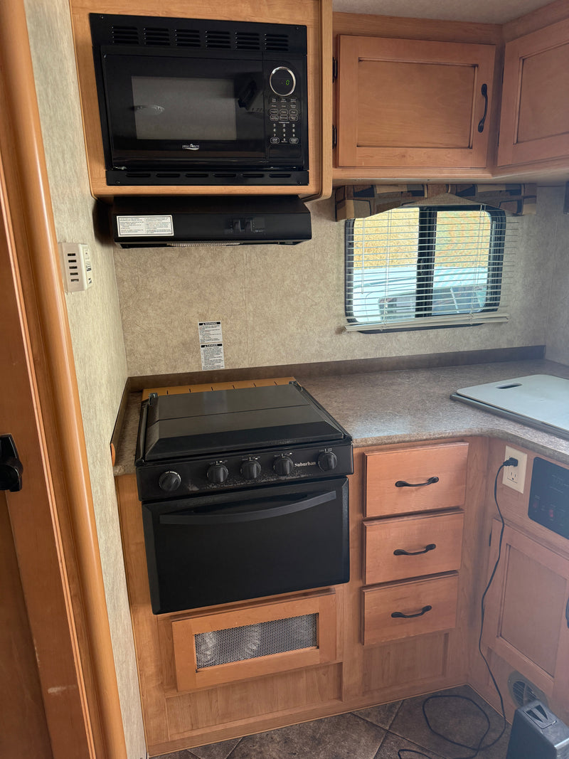 Well-equipped RV rental kitchen featuring a microwave, Suburban stove/oven, wooden cabinets, and a window. — photo 12