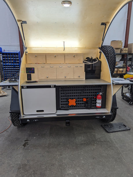 RV rental teardrop trailer outdoor kitchen setup. Features include fridge, storage, power, and fire extinguisher for safe adventure.