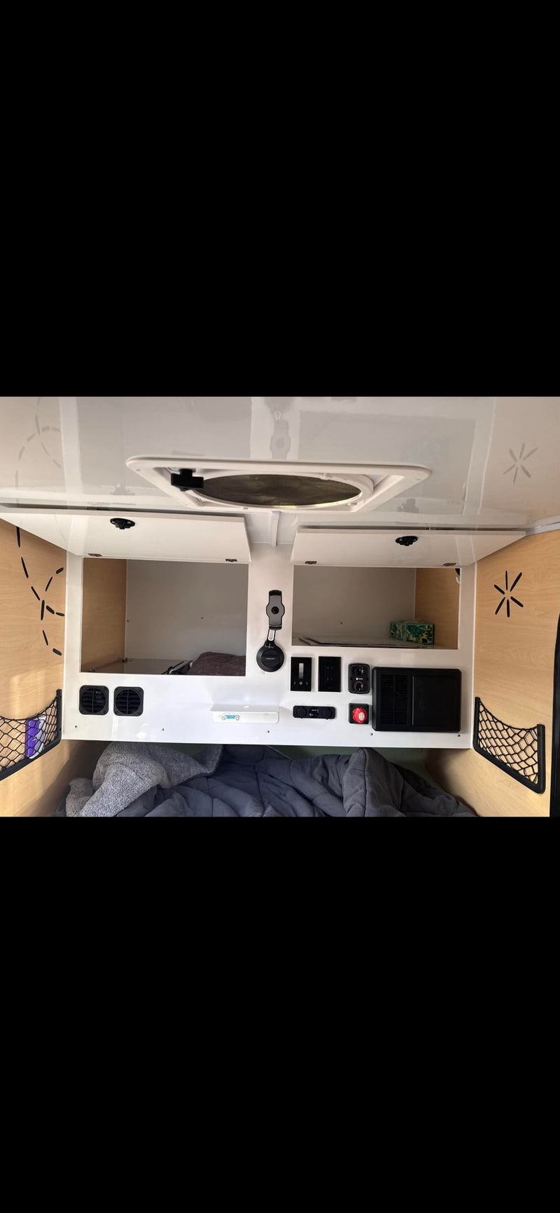 Inside a cozy RV rental: gray bedding, overhead storage, and a control panel with outlets. A compact camper interior for your trip. — photo 6