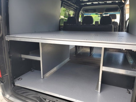Spacious RV rental interior with an elevated bed platform and organized storage compartments for gear and supplies.