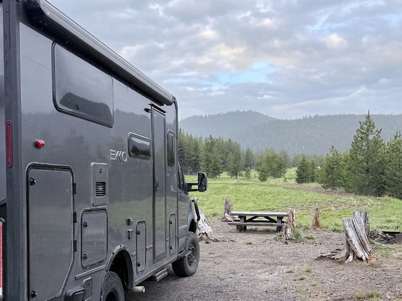  is parked overlooking a beautiful ocean sunset with sea stacks.|Rugged grey RV rental camper van parked in a sunlit forest — photo 3