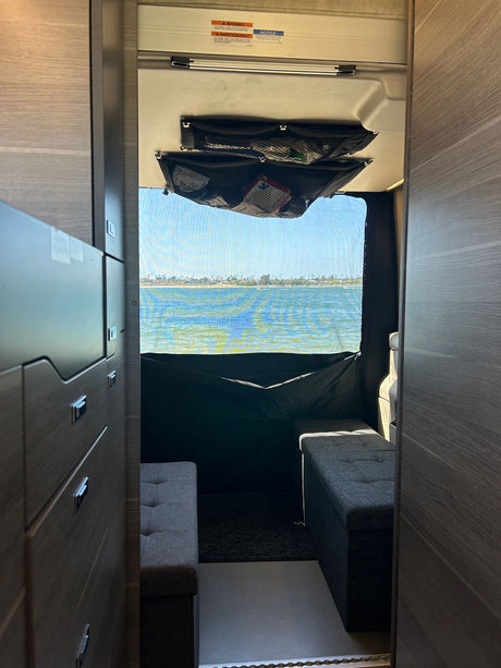 An RV rental interior with compact living, cabinetry, benches, overhead storage, and a beautiful bay view.