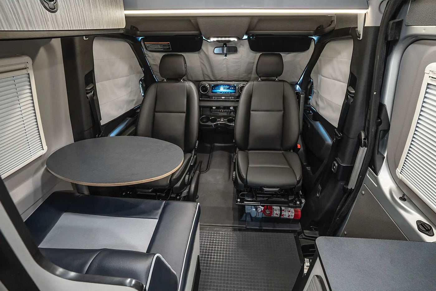  and window view.|Inside an RV rental: Compact interior showing the driver's cabin with two seats and a rear dining area with a round table.|This Winnebago Revel camper van — photo 6