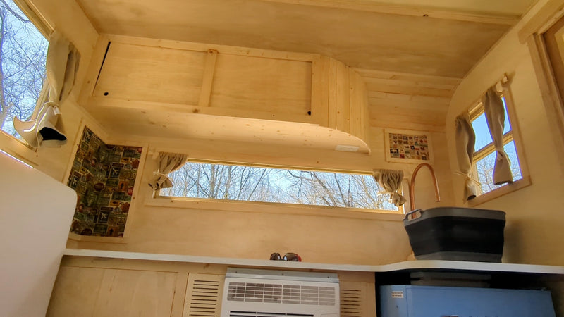 Inside an RV rental: light wood interior, functional kitchen with copper faucet & sink, AC unit, and forest views from windows. — photo 7