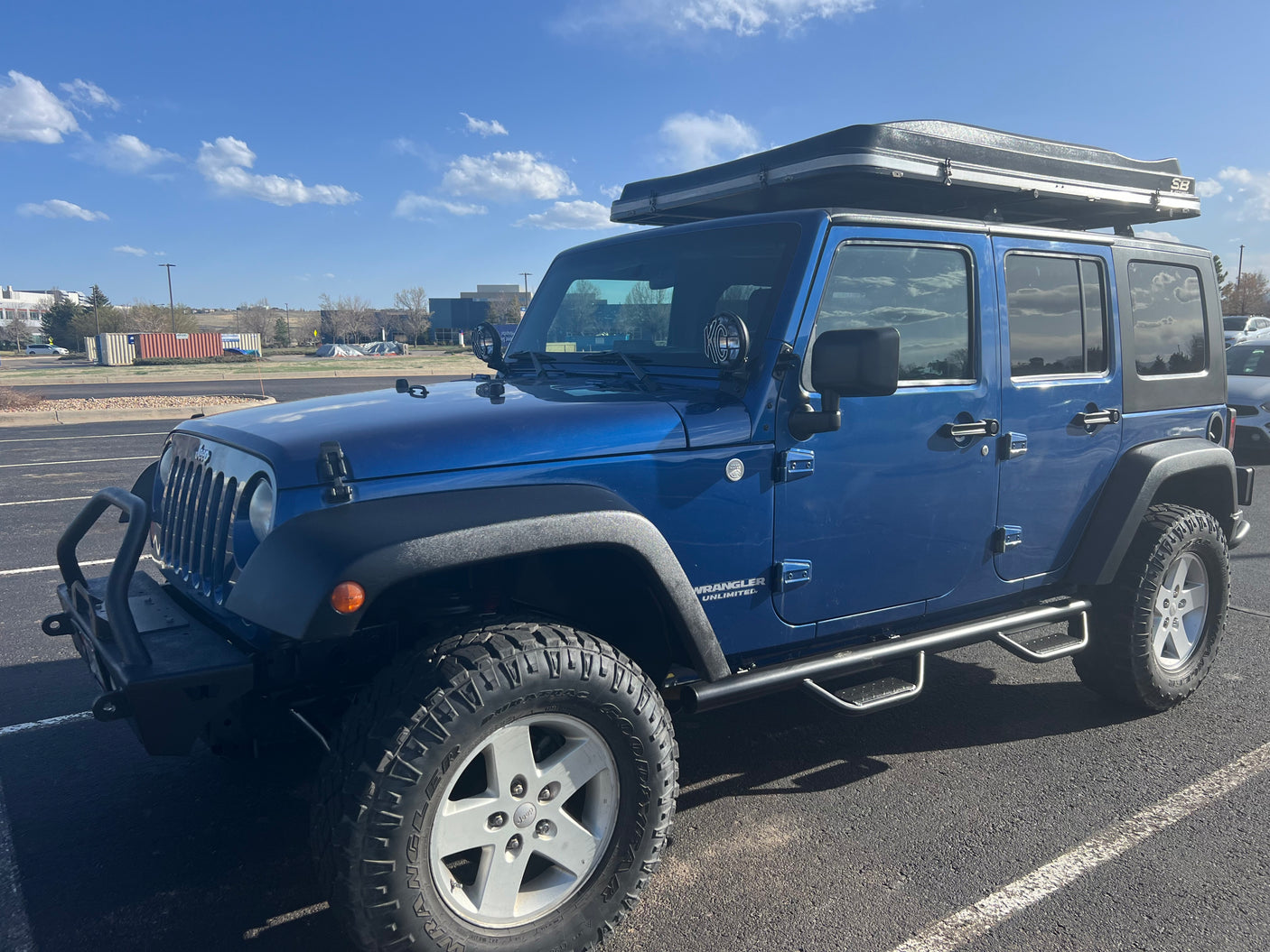 Blue Jeep Wrangler Unlimited with hard-shell rooftop tent, great for outdoor adventure or RV rental camping.