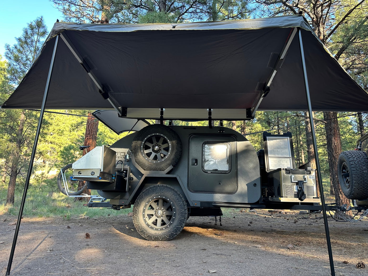 Dark grey overland trailer with awning & outdoor kitchen set up in a pine forest. Great option for an rv rental. — photo 2