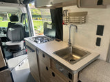 This rv rental features a well-equipped kitchen with a two-burner stove, sink, and counter space, alongside the front passenger seat.