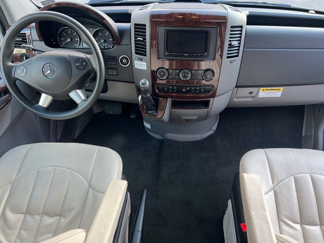 **RV rental**: Front cabin view with Mercedes-Benz steering wheel, wood-trimmed dashboard, and light-colored seats.
