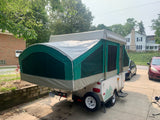 A green and white pop-up camper, a type of RV, is fully extended in a sunny driveway. Consider for rv rental.