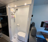 RV rental interior: compact wet bath with shower and portable toilet. Adjacent microwave and mini-fridge.