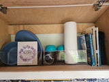 Organized RV cabinet with Hawaii travel books, blue plates, and kitchen essentials for your RV rental.
