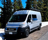 A white Ram camper van, equipped for adventure, parked in snowy mountains. Consider this RV rental for your next trip.