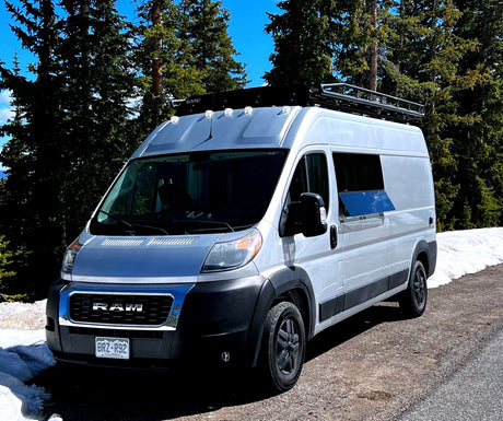 A white Ram camper van, equipped for adventure, parked in snowy mountains. Consider this RV rental for your next trip.