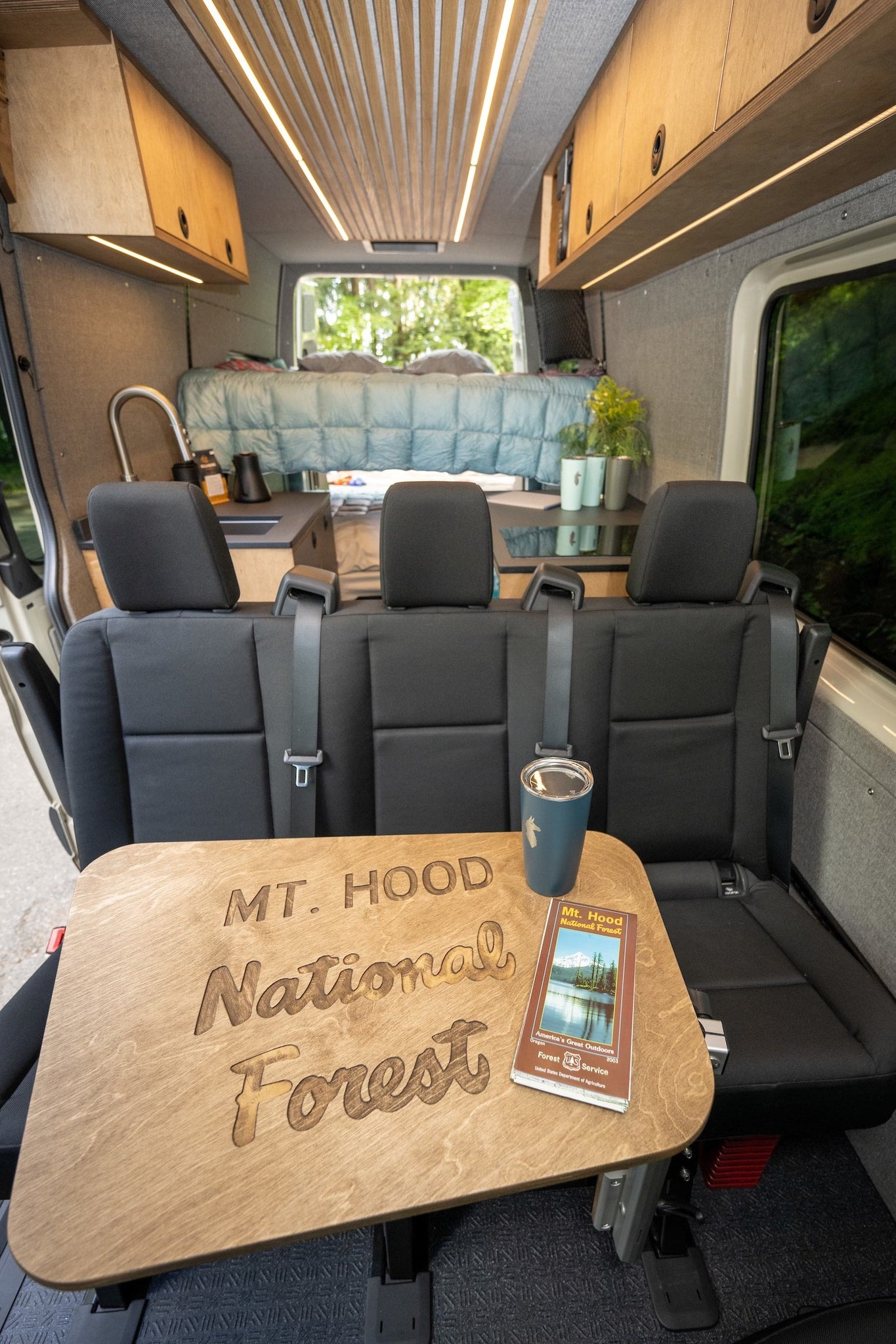 RV rental's inviting interior: Custom table with 'Mt. Hood' engraving, comfortable bed, and wood-slat ceiling. — photo 7