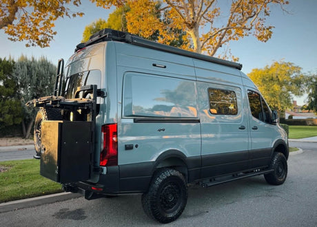 Adventure-ready gray camper van with off-road tires, roof rack & rear storage. Perfect for your RV rental journey.