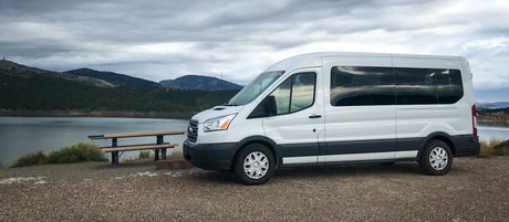 White RV rental van at a scenic lake, mountains & cloudy skies. Perfect for road trips & outdoor adventures!