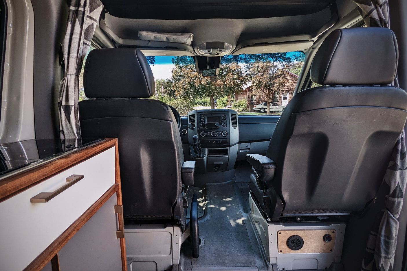 RV rental: Inside a customized camper van, view from the rear. Shows front seats, dashboard, and built-in kitchenette.