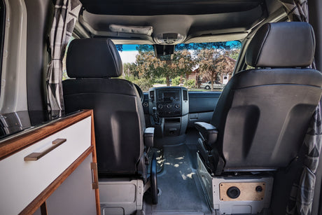 RV rental: Inside a customized camper van, view from the rear. Shows front seats, dashboard, and built-in kitchenette.